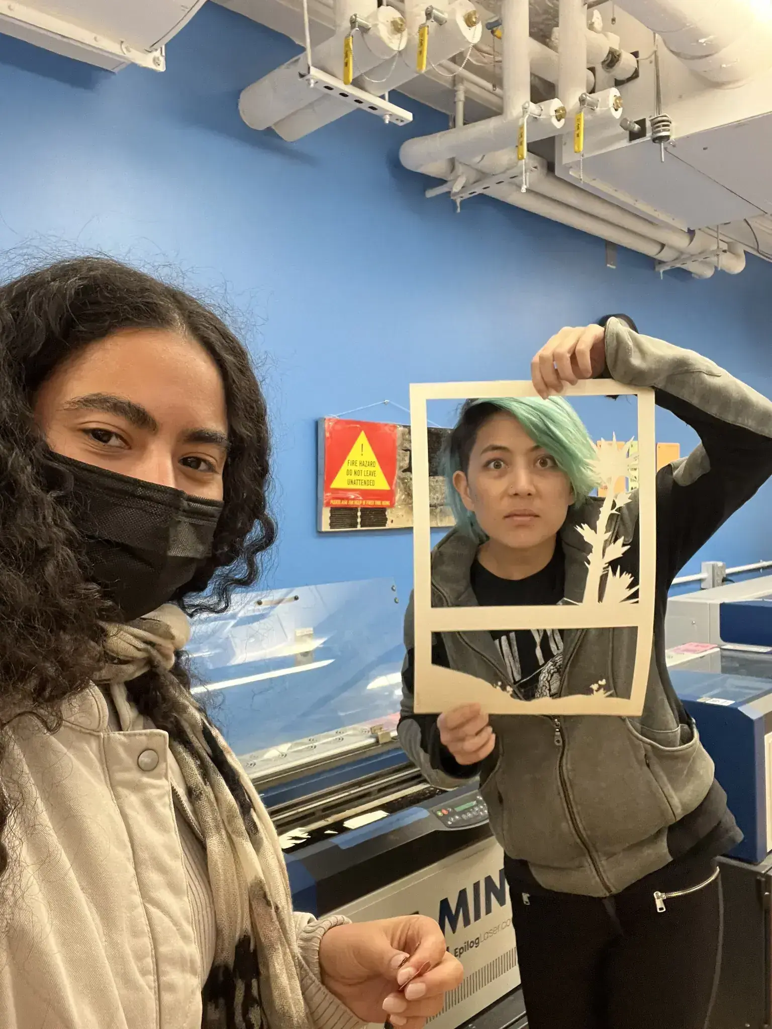 Photograph of two girls making funny faces while holding up laser cut papers like a picture frame