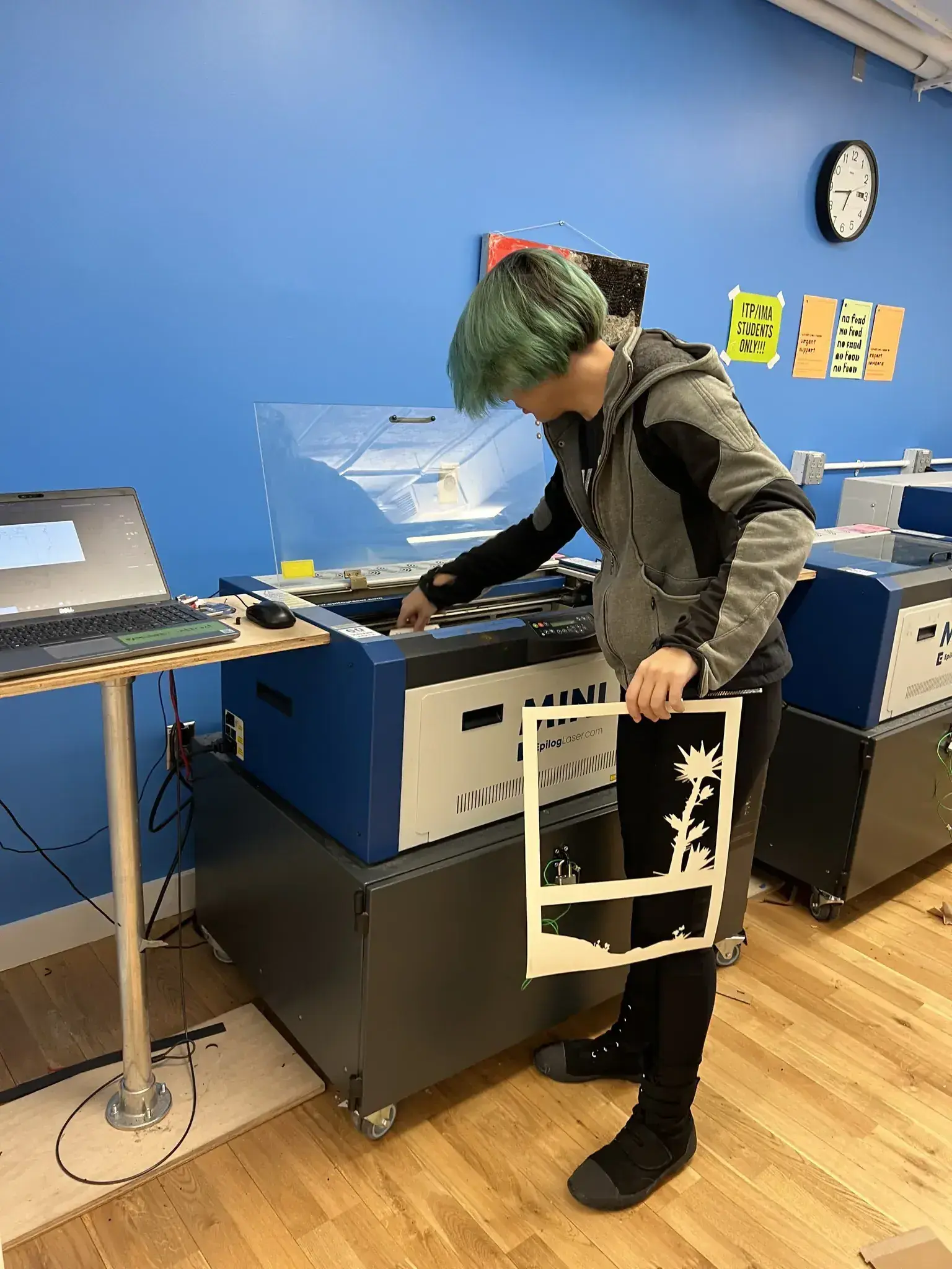 Photograph of a green haired woman waiting for the laser cutter