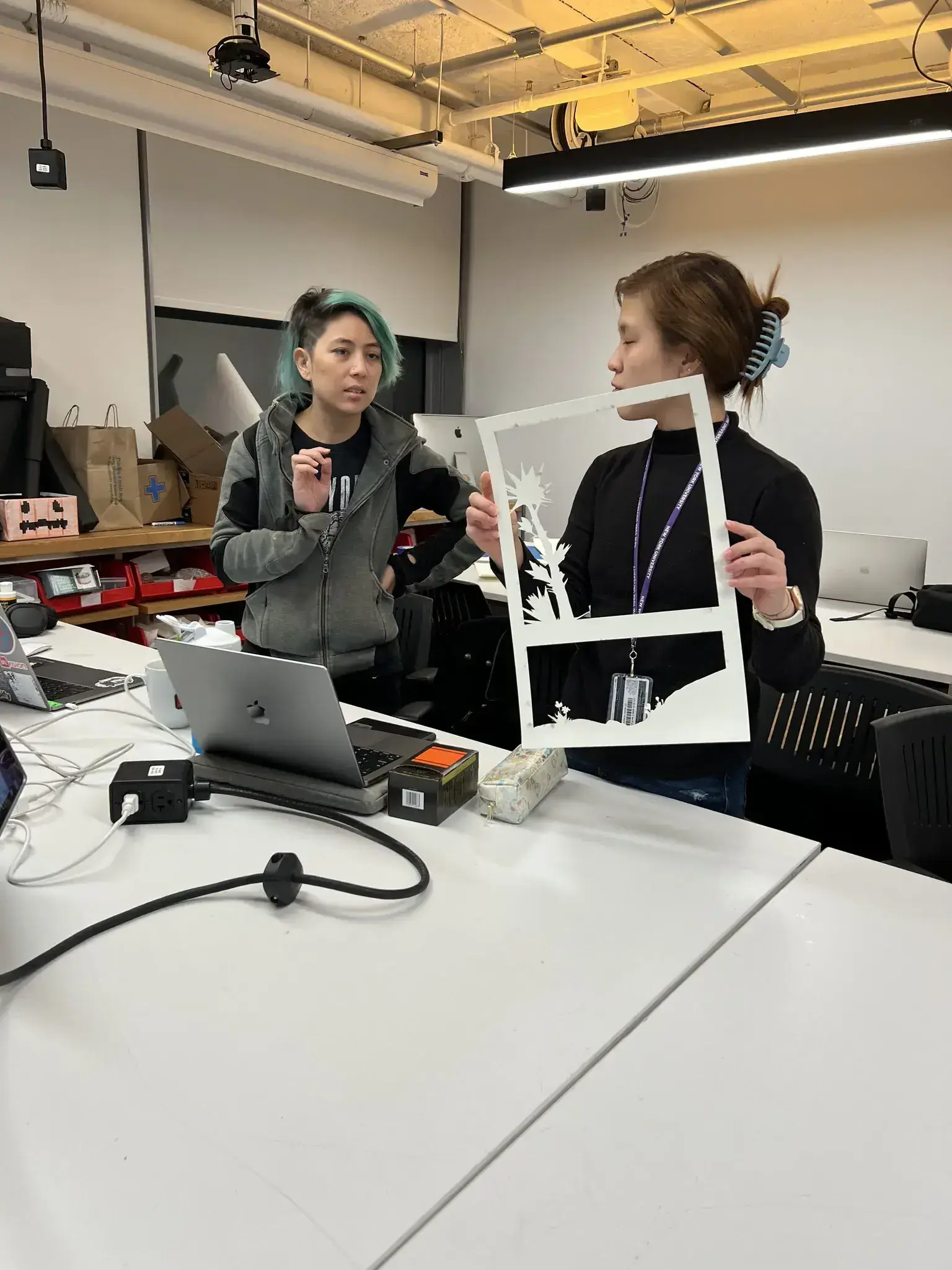 Two women discussing the construction of the book while holding up layers