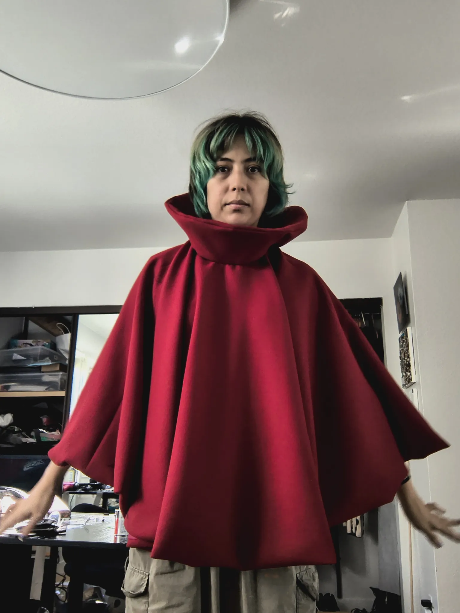 Wearing the finished red cloak with the high standing collar, arms out, without the mask