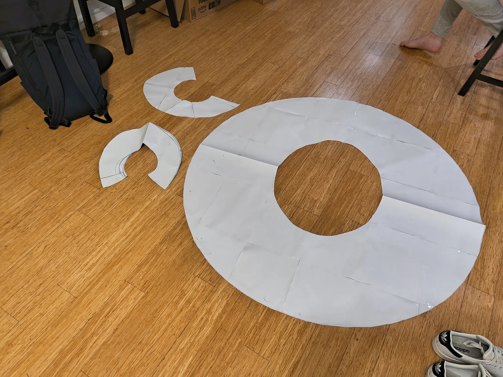 A paper pattern for a circular cloak laid out on a wooden floor, a large ring with the neck hole in the middle and three curved collar pieces beside it