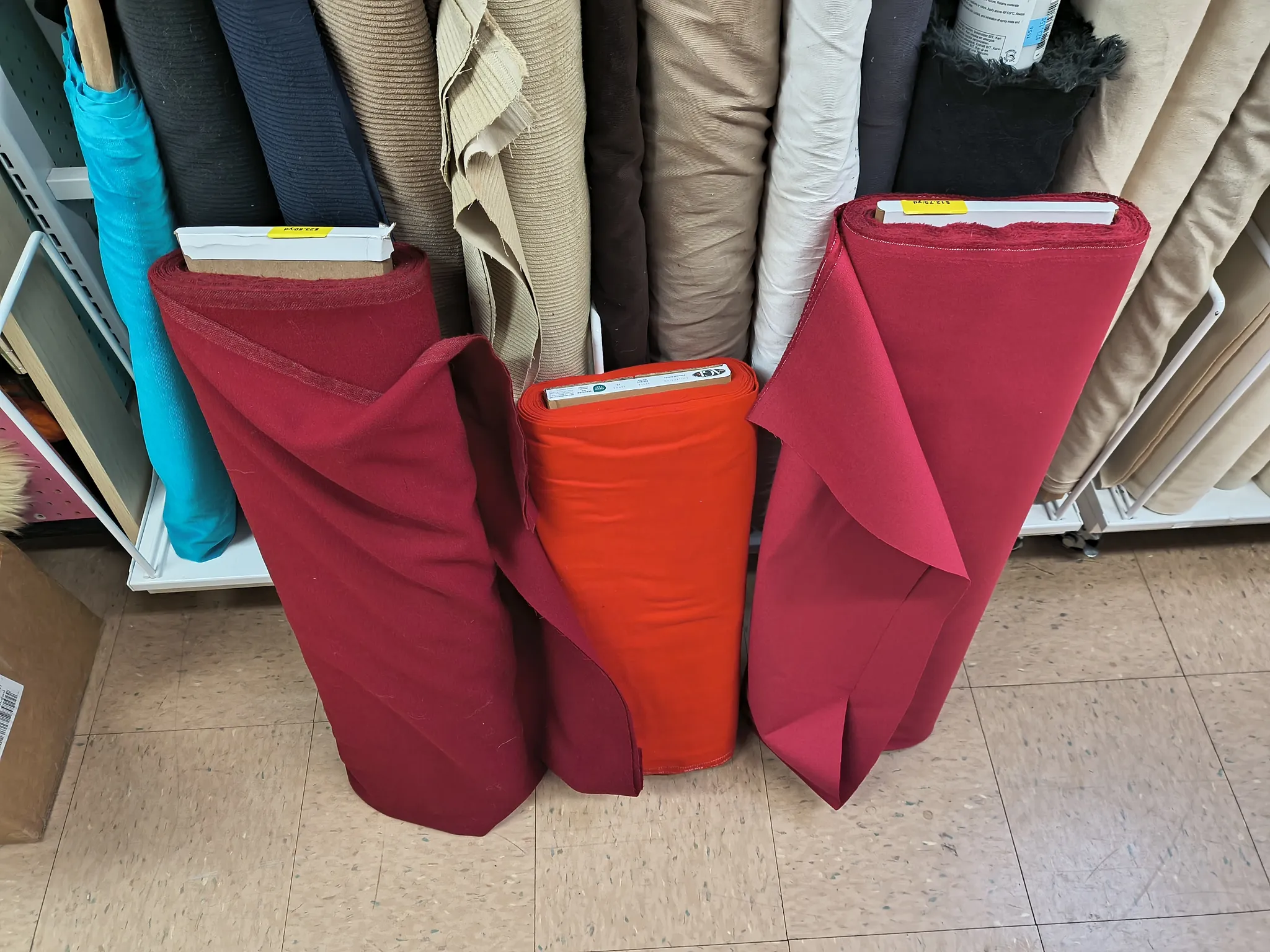 Three bolts of red fabric in slightly different shades and weights leaning against the shelves at a fabric store