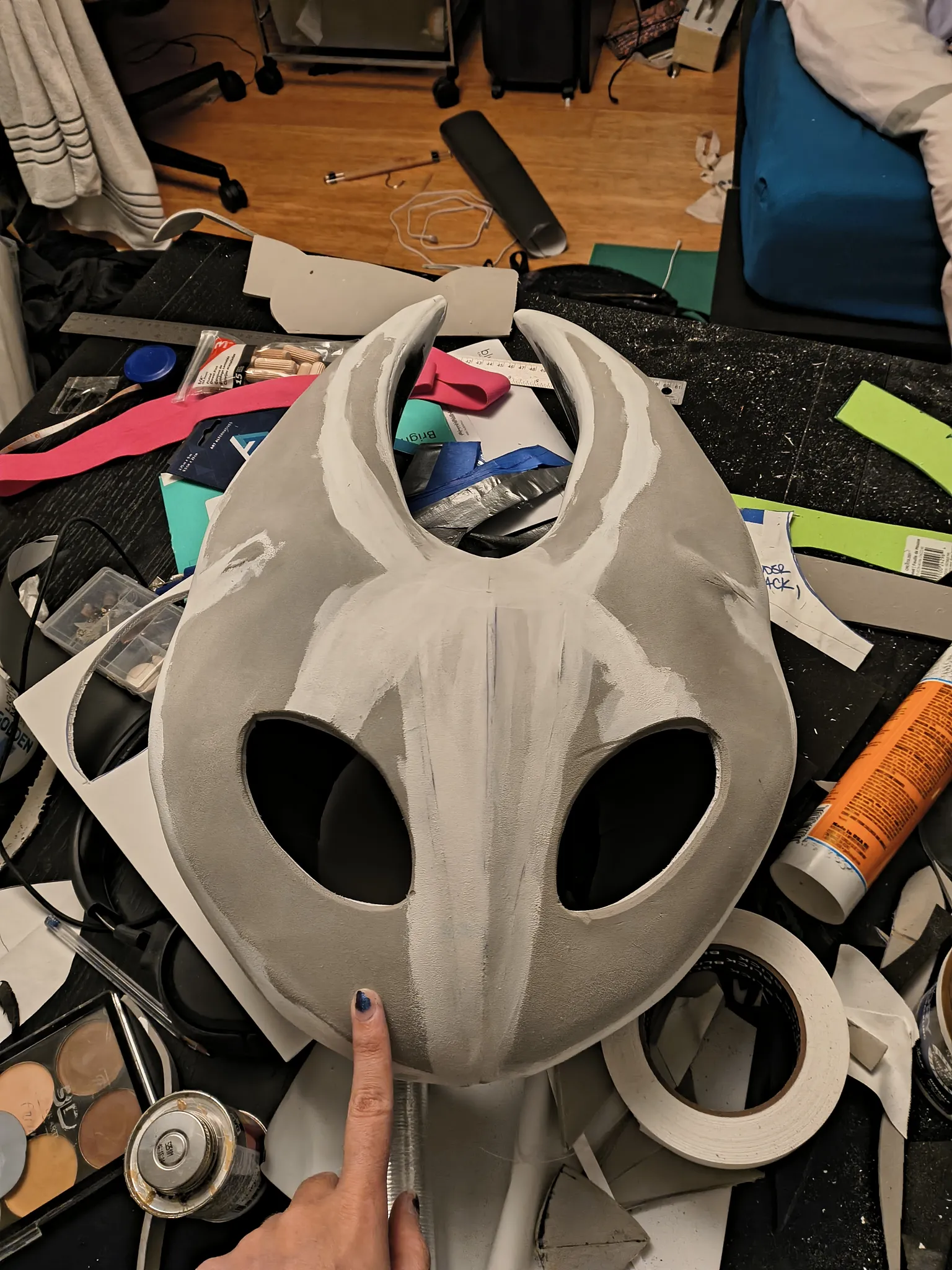 The foam mask with white gesso brushed over the seams and the spackle patches, sitting on a desk covered in tools