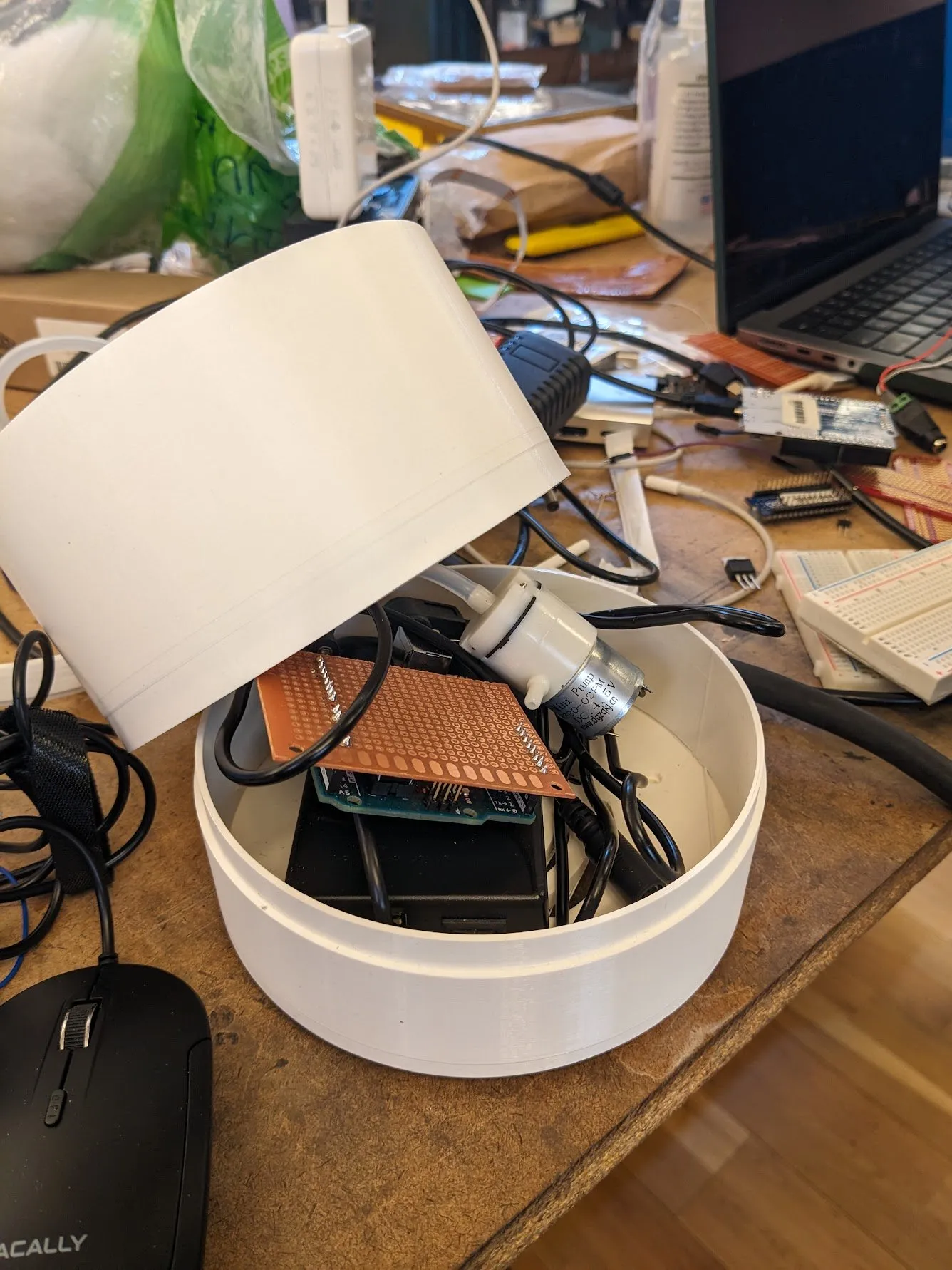 The white 3D printed enclosure with its lid tilted off, revealing the wiring, power board, and ultrasonic module packed inside, sitting on a cluttered desk.