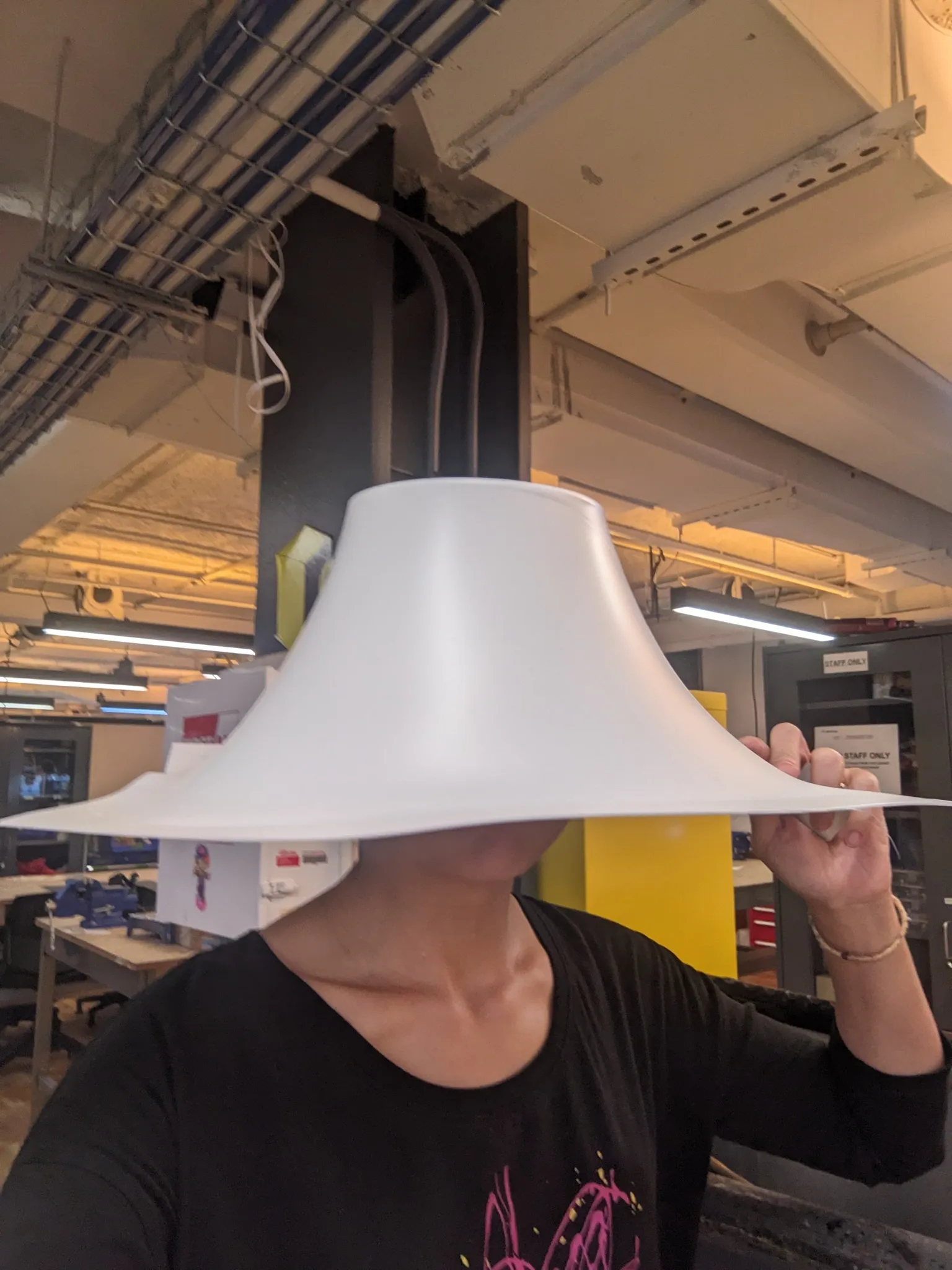 A person in the shop holding a large, wide-brimmed vacuum formed white plastic shell over their face like a hat.