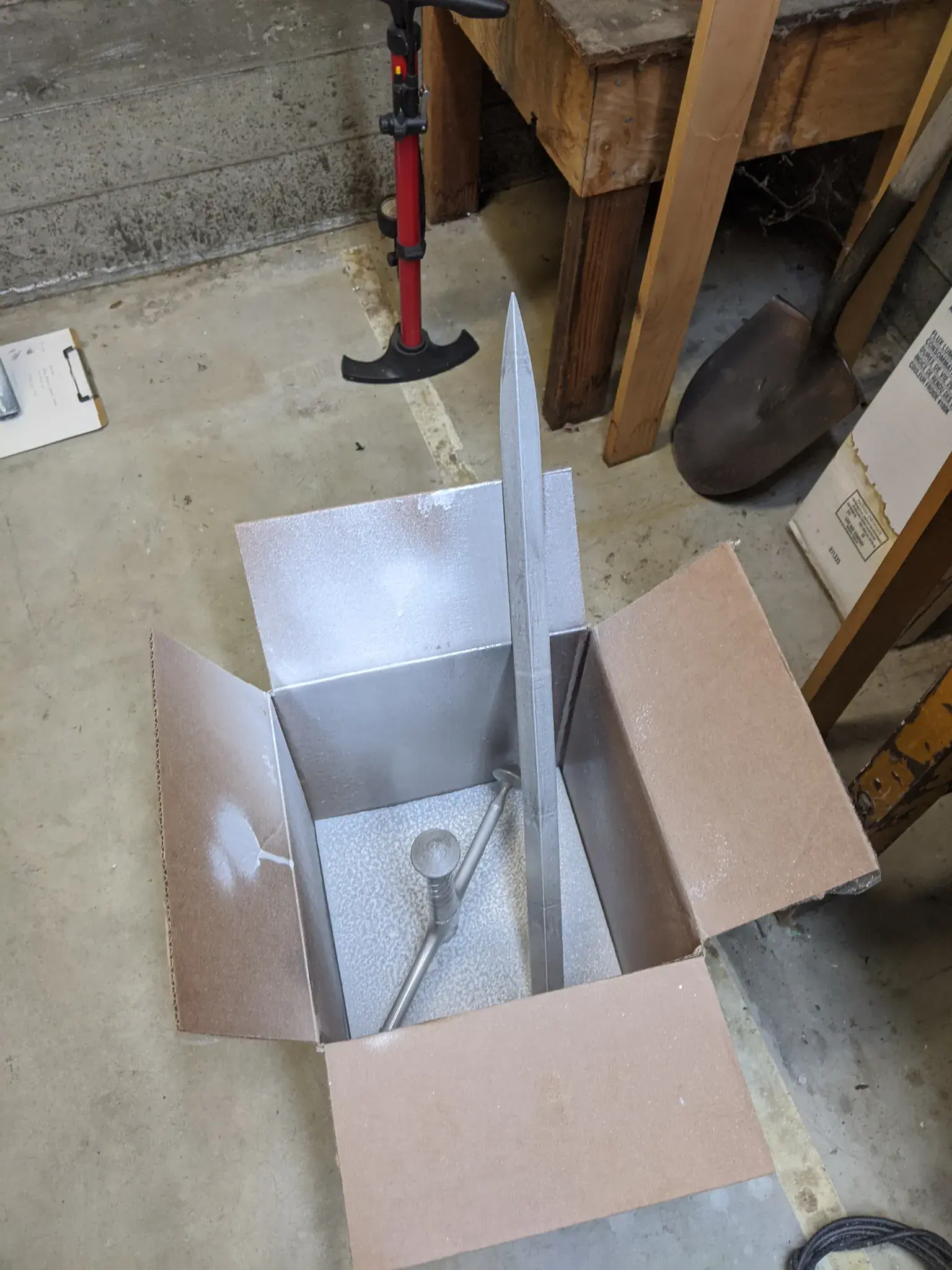 Photograph of pieces of a sword sitting in a box freshly coated with silver paint