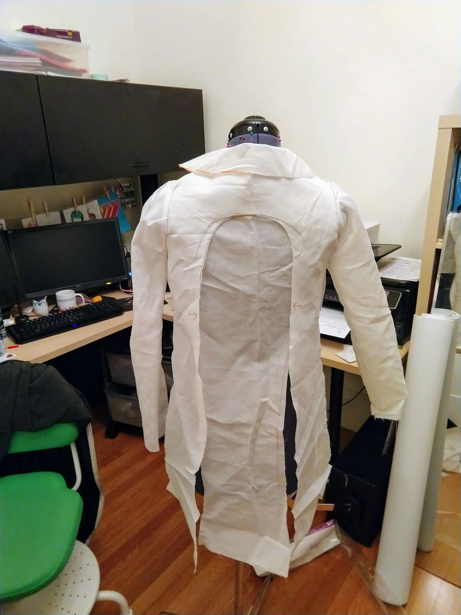 Photograph of a mannequin from the back with white muslin fabric shaped into a jacket with tails