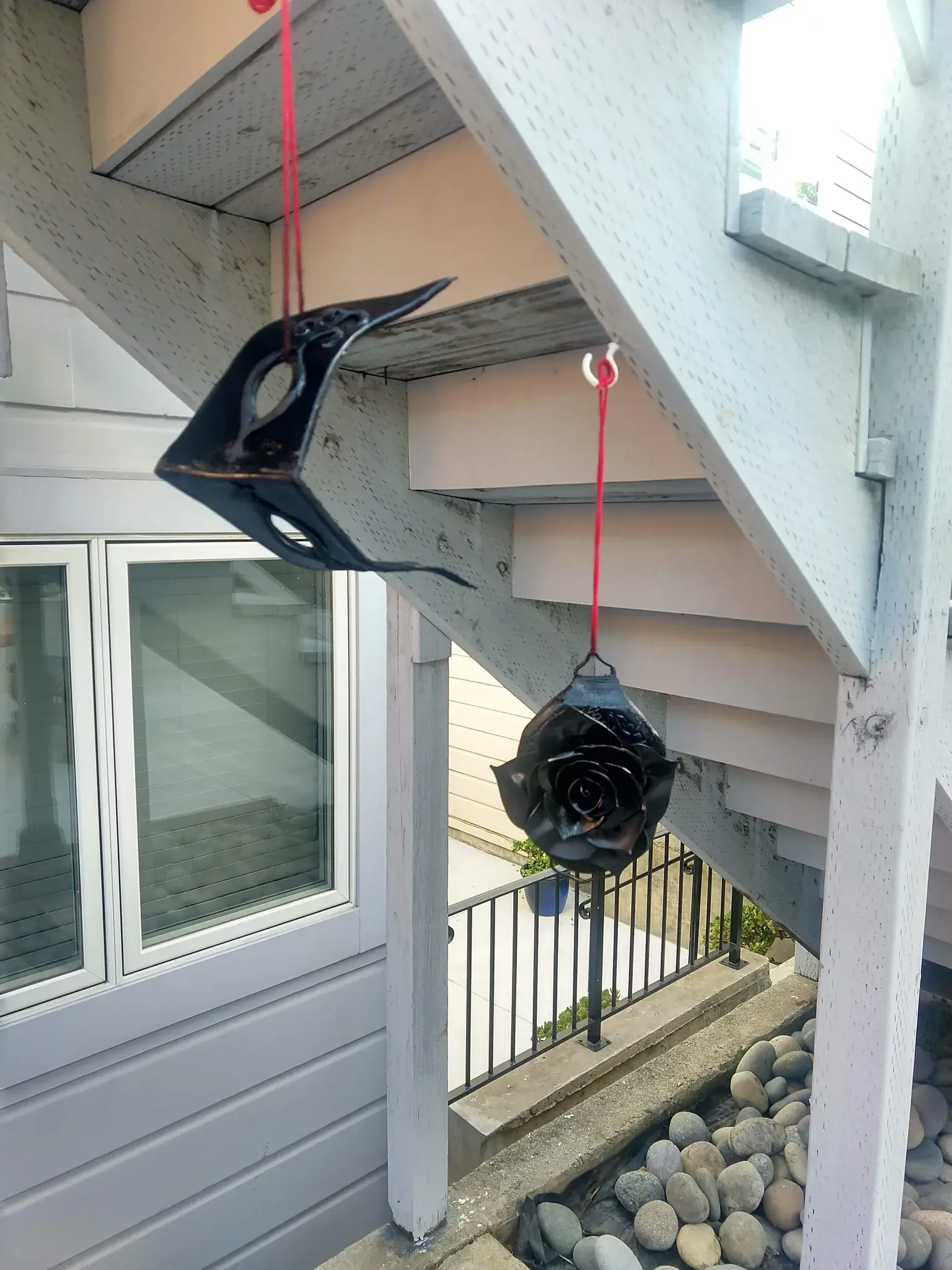 Photograph of a belt and mask covered in shiny black coating hanging from a staircase