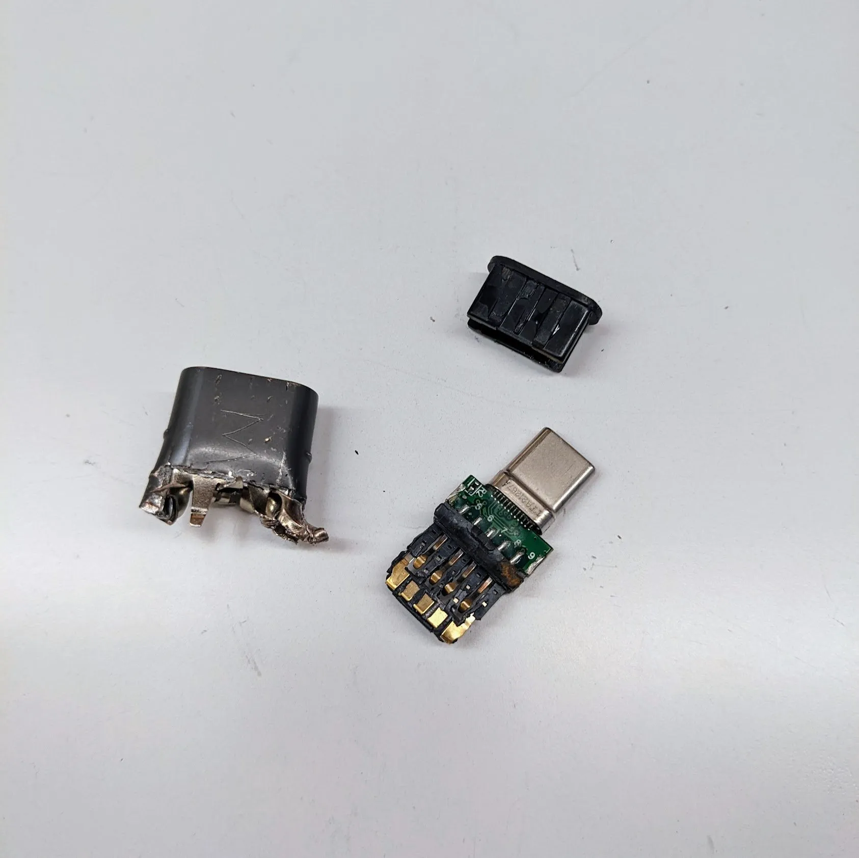 The sacrificed adapter taken apart on a white surface: the metal shell, the plastic housing, and the small green circuit board with the USB-C connector still attached.