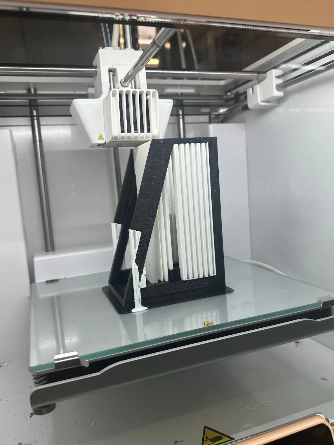 The black frame partway through printing on the bed of an FDM printer.