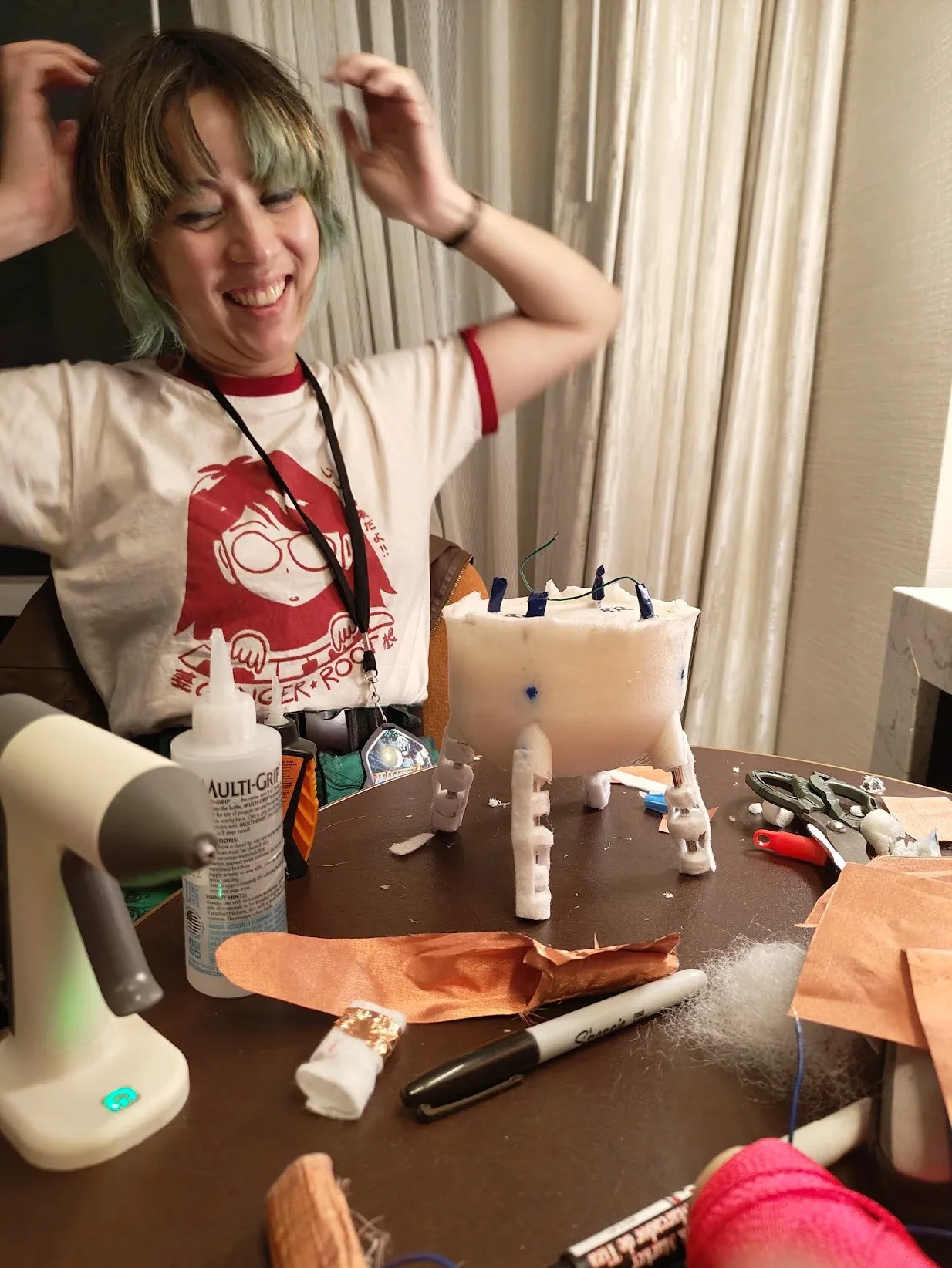Photograph of Karina laughing at a hotel room table with the foam udder core in front of her, its sensor wires poking out the top